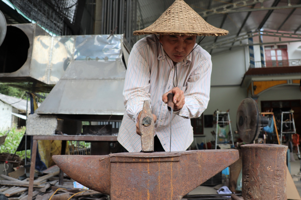 Traditional blacksmiths hammering red-hot iron at a workshop in Phuc Sen